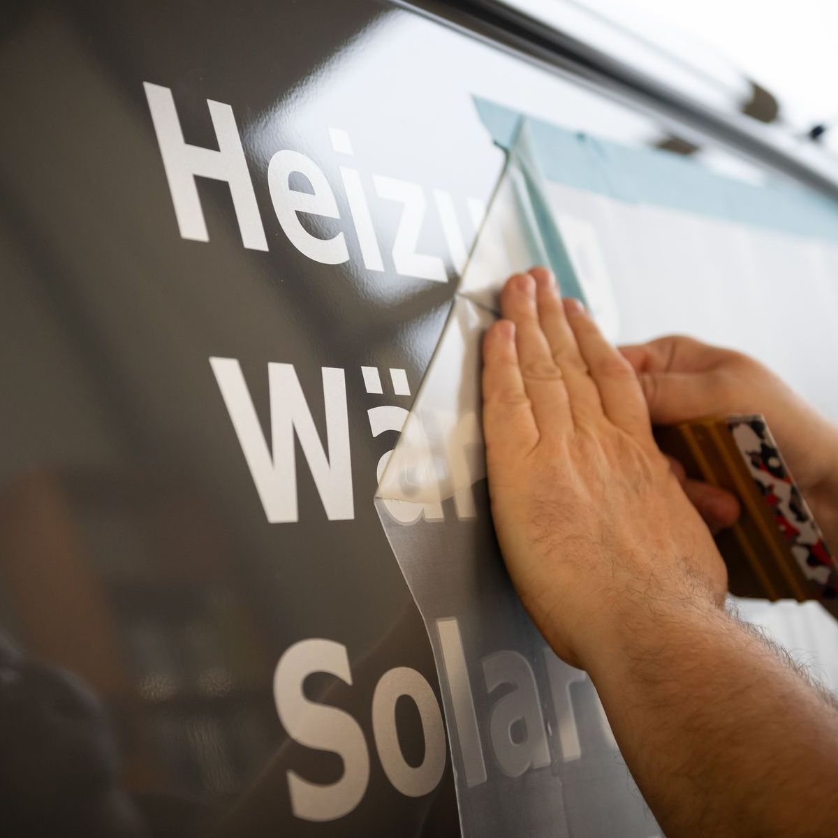 Man sieht Hände eines Mitarbeiters der Druckerei Dahler Print beim Aufbringen von geplotteten Schriftzügen auf einen Transporter.