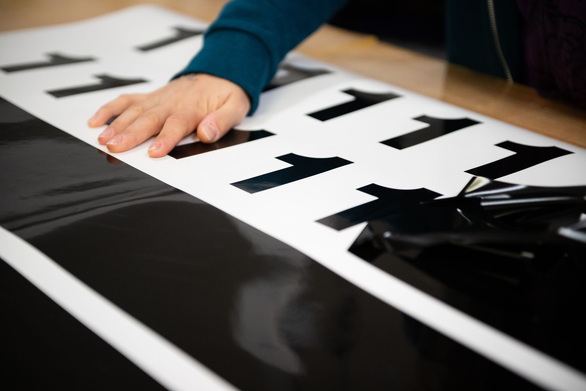 Eine Mitarbeiterin der Druckerei Dahler Print zieht fertig geplottete Folie ab. Man sieht als Ergebnis auf der einen Seite schon mehrere Einsen in schwarz.