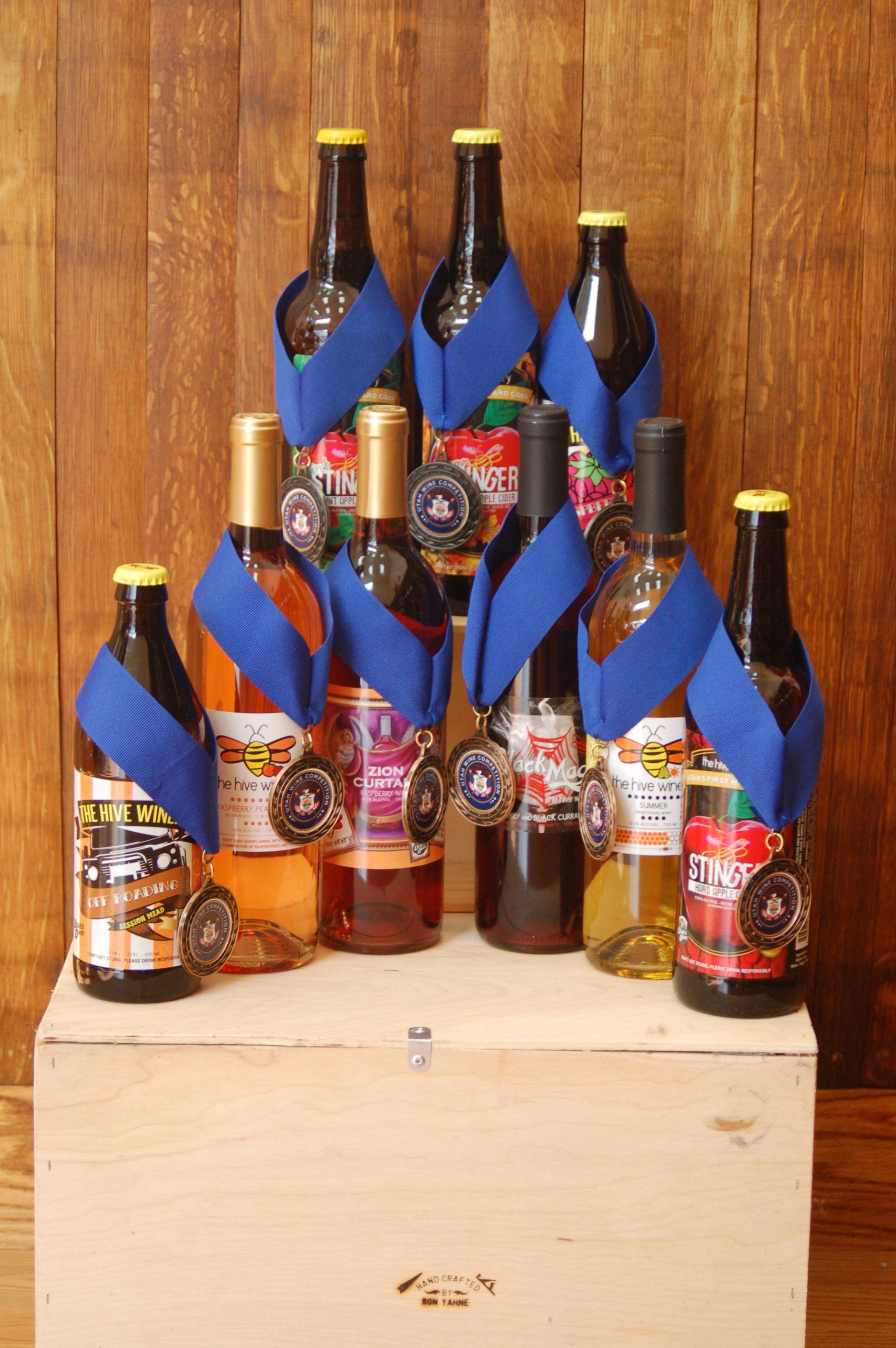 Bottles of fruit wine, hard cider, and session mead set against a wooden  background each bottle with and award ribbon.
