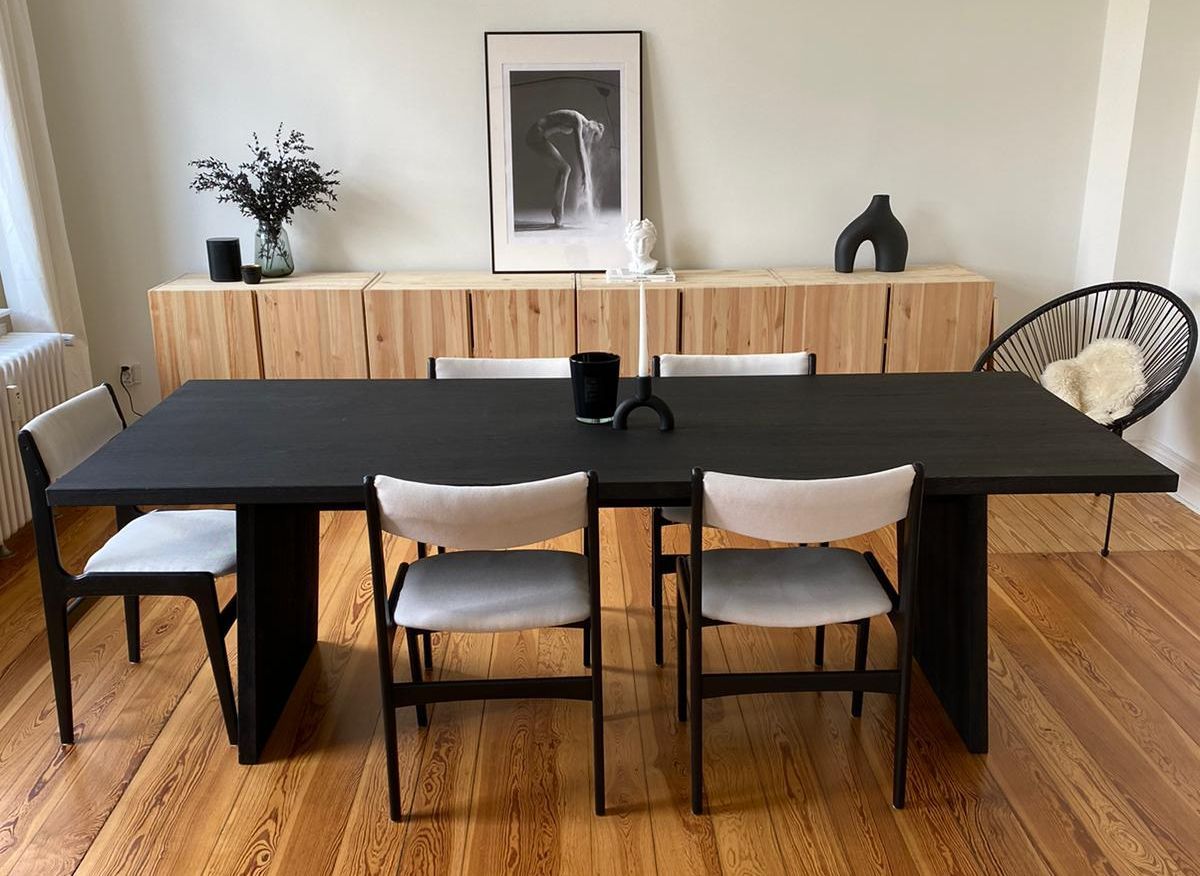 Esstisch der BLACK OAK Kollektion von JANUFAKTUR in einer hellen Altbauwohnung mit schwarzen Polsterstühlen und Dekoration.