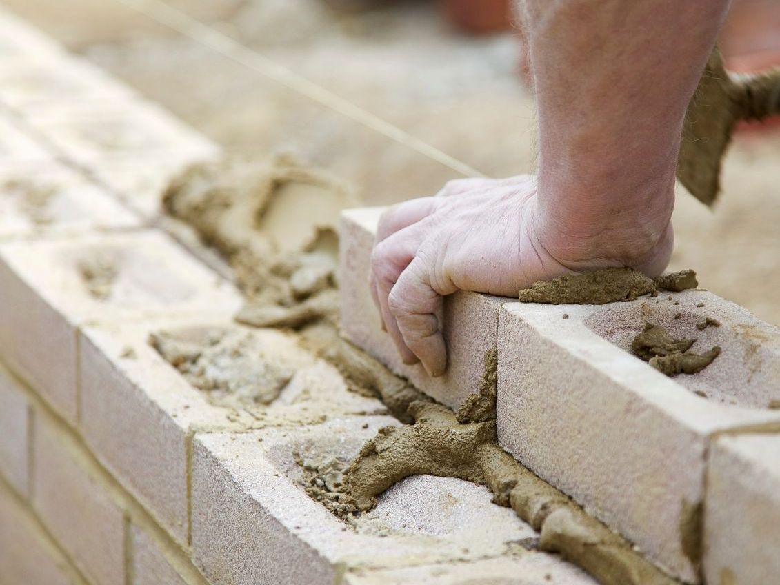 Bauarbeiter setzt einen Stein mit Mörtel auf eine Mauer