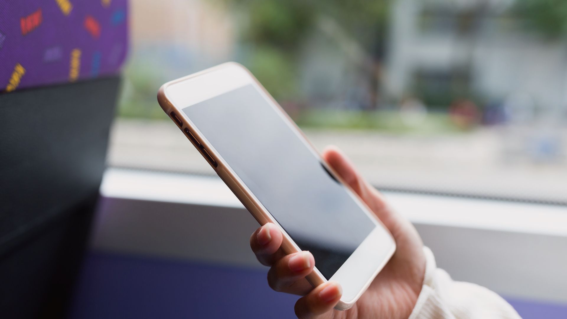 Primo piano di una mano che tiene uno smartphone vicino al finestrino di un autobus.