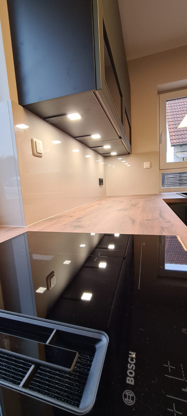 Das Bild präsentiert eine exquisite Nobilia Küche mit grifflosen Schränken, deren Schönheit durch die EASYTOUCH 964 Mineralgrün ultramatten Fronten hervorgehoben wird. Diese Küchenecke wurde mit Bedacht gestaltet, um eine einladende Oase zu schaffen, die besonders für entspannte Kaffeemomente am Morgen geeignet ist. Die elegante Bosch accentline Einbaugeräte-Serie in edlem Schwarz passt perfekt zum Gesamtdesign und bietet zudem innovative Funktionen für ein erstklassiges Kocherlebnis. Die LED-Beleuchtung, die die Einbauküche umgibt, setzt die Küche ins rechte Licht und verleiht ihr eine warme, einladende Atmosphäre, die das Kochen und Genießen zu einem wahren Vergnügen macht.