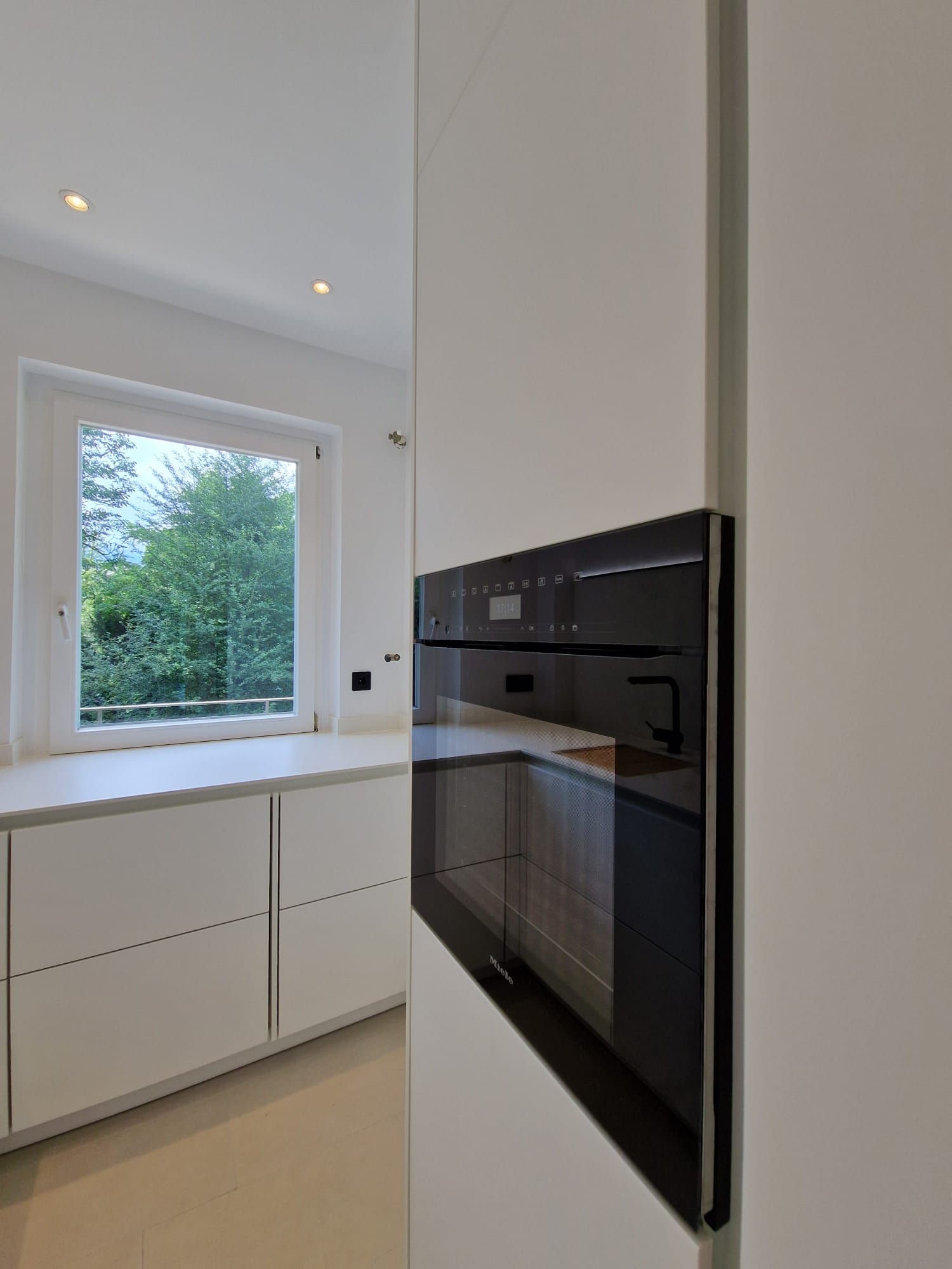 Die luxuriöse Ballerina Einbauküche im Herzen Frankfurts besticht durch ein schneeweißes Design, elegante schwarze Akzente und eine markante schwarze Lofttür, die als moderner Blickfang den Raum abrundet – ergänzt durch Bosch Geräte und einen grifflosen Miele Backofen.