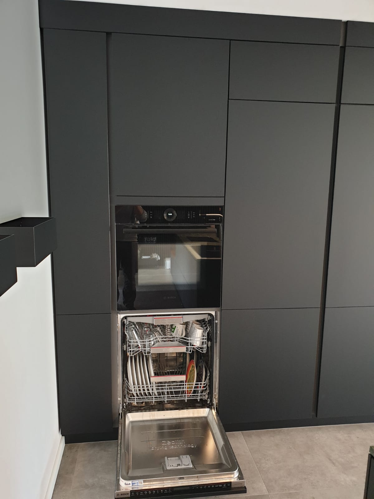 Entdecken Sie die perfekte Verbindung von Eleganz und Innovation mit unserer Nobilia Einbauküche, die mit Antifingerprint Fronten in Schwarz, einer Natursteinarbeitsplatte von Strasser in Alpengrün im Leather-Look und hochmodernen Einbaugeräten von Bosch AccentLine ausgestattet ist, um Ihrem Zuhause einen Hauch von Luxus zu verleihen.