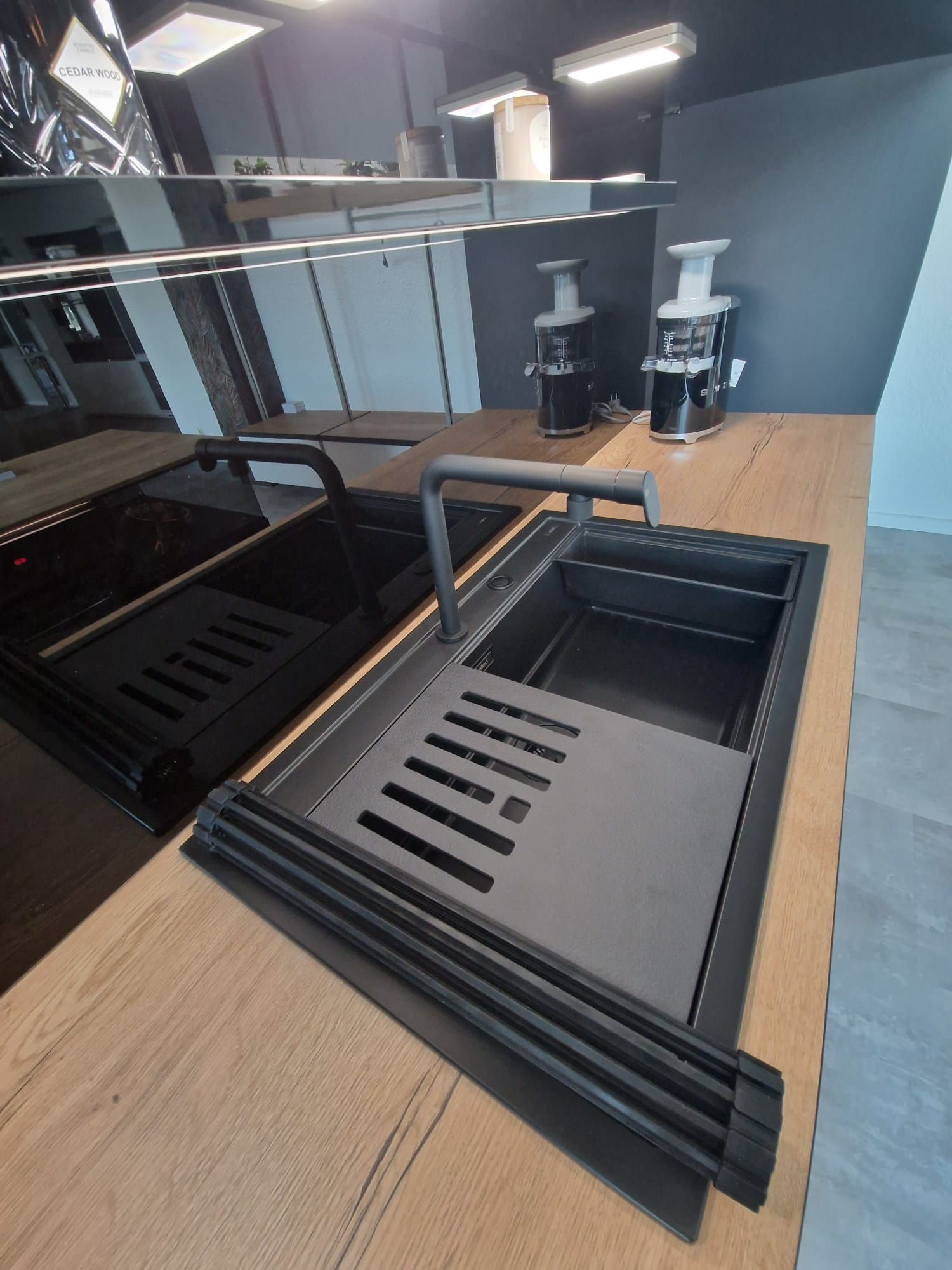 Erleben Sie die Vielseitigkeit unserer Einbau-Musterküche, die mit einem ganz schwarzen Design, einer Keramik-Arbeitsplatte in Holzoptik und einer eleganten Vitrine für Gläser eine harmonische und moderne Ästhetik verkörpert.