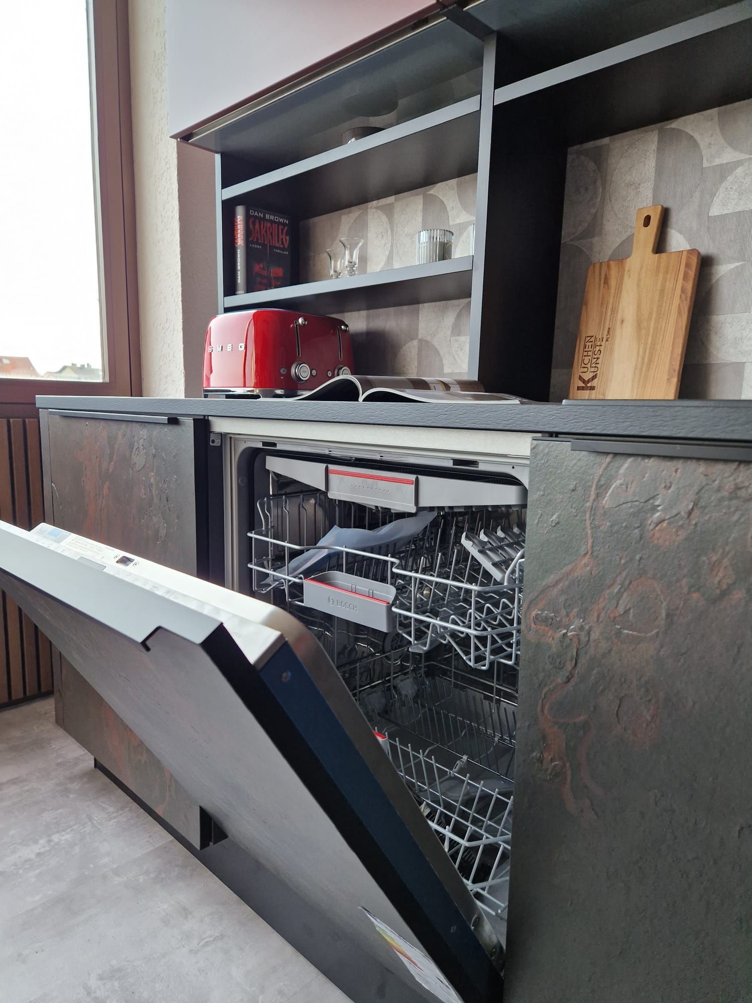 Verleihen Sie Ihrer Küche mit unserer Nolte Neo Einbau-Musterküche eine exklusive Note. Die Berbel Skyline Dunstabzugshaube, die Fronten in Schiefer-Schwarz Rosato und Henarot Softlack sowie die beleuchteten Hängeschränke mit elektrischer Öffnung sind wahre Highlights dieser Küche.