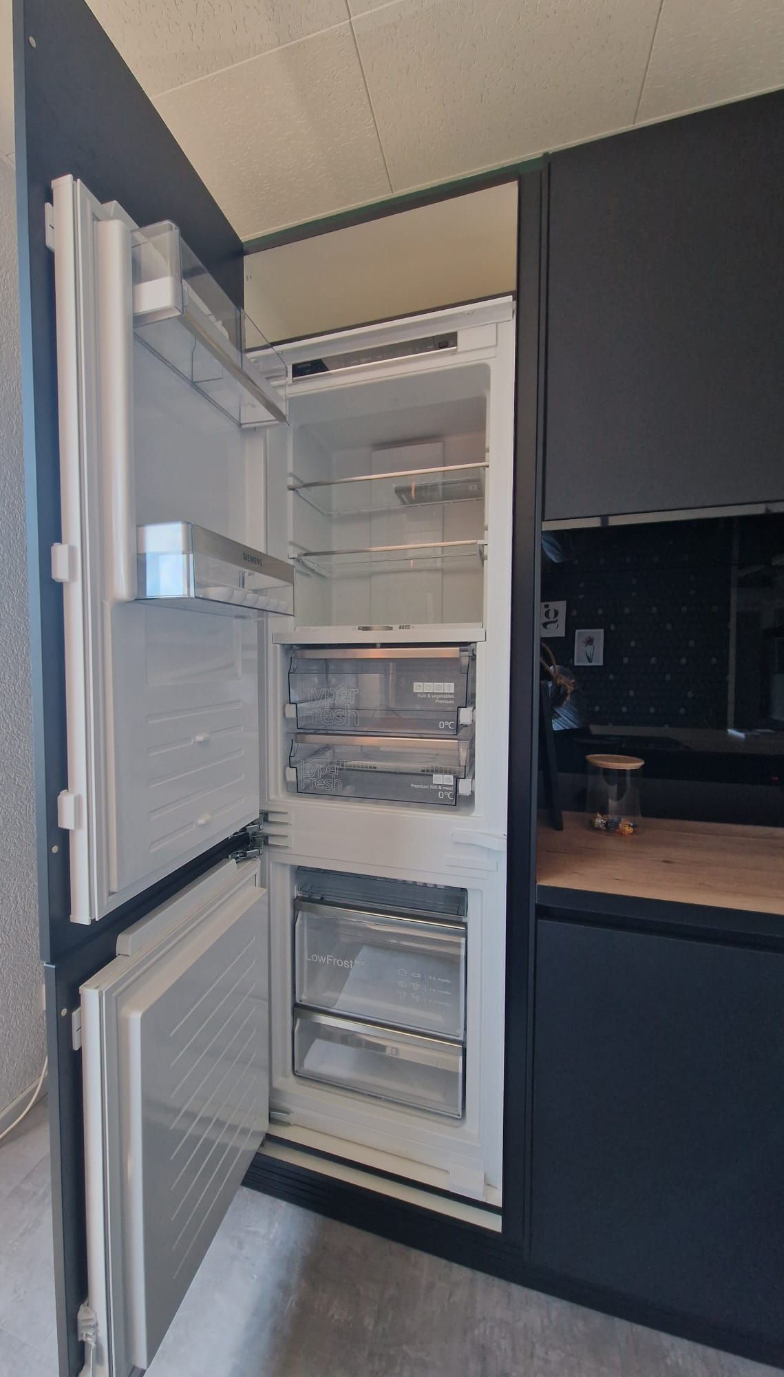 Mit unserer Einbau-Musterküche in Schwarz setzen Sie auf zeitlose Eleganz und modernes Design, während die Keramik-Arbeitsplatte in Holzoptik und die elegante Vitrine für Gläser für eine individuelle Note sorgen.