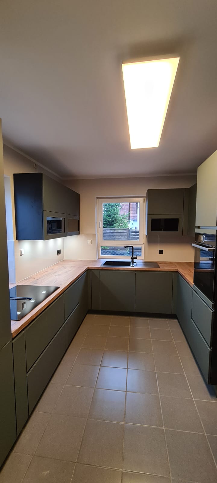 Das Bild zeigt eine geschmackvolle Nobilia Küche mit grifflosen Schränken, die mit den exquisiten EASYTOUCH 964 Mineralgrün ultramatten Fronten veredelt sind. Diese Küchenecke strahlt eine einladende Atmosphäre aus und lädt dazu ein, den Tag mit einer Tasse Kaffee zu beginnen. Die Bosch accentline Einbaugeräte in Schwarz ergänzen das ansprechende Design perfekt und bieten gleichzeitig erstklassige Leistung und Funktionalität. Diese Küche ist nicht nur ein Ort zum Kochen, sondern auch ein Ort, an dem man gerne Zeit verbringt und die morgendliche Ruhe genießt.