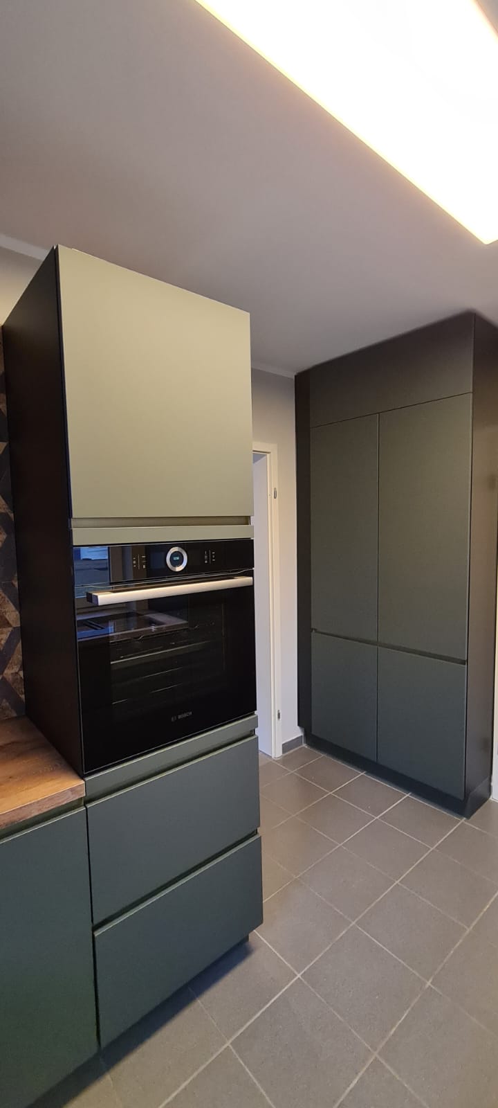 Auf dem Bild ist eine moderne Nobilia Küche zu sehen, die mit grifflosen Schränken und EASYTOUCH 964 Mineralgrün ultramatten Fronten ausgestattet ist. Die Gestaltung dieser Küchenecke erinnert an eine Oase, die speziell für entspannte Kaffeemomente am Morgen geschaffen wurde. Die eleganten Bosch accentline Einbaugeräte in Schwarz passen perfekt zum Design und setzen stilvolle Akzente, die die Mineralgrünfronten der Küche hervorheben. Diese Küche lädt zu genussvollen Start in den Tag ein und strahlt dabei eine zeitlose Eleganz aus.