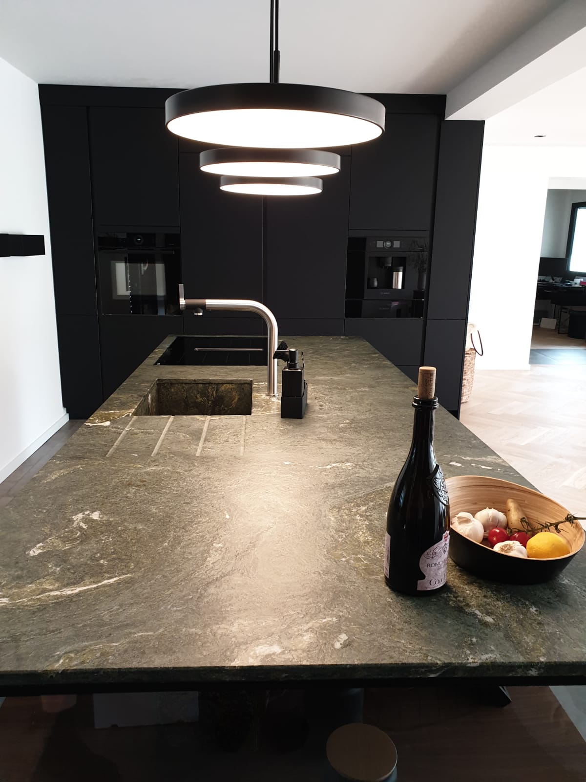 Tauchen Sie ein in die dunkle Eleganz unserer Nobilia Einbauküche mit Antifingerprint Fronten in Schwarz, die mit einer Natursteinarbeitsplatte von Strasser in Alpengrün im Leather-Look einen Hauch von Raffinesse verleiht.