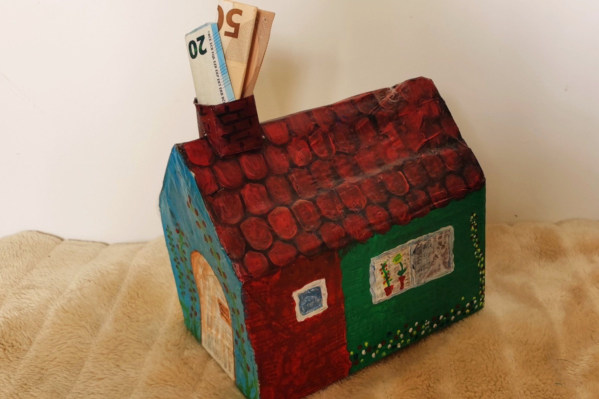 Ein buntes Haus, in dessen Schornstein zwei Geldscheine stecken.