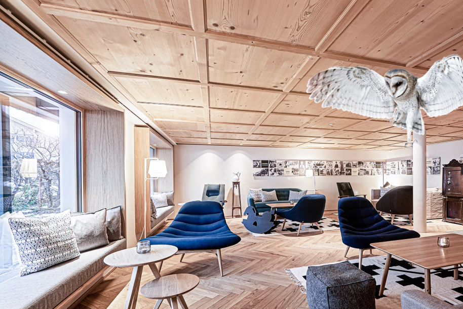 Stilvoller Wohnraum mit warmem Holzparkett, blauen Design-Sesseln und gemütlicher Alpen-Atmosphäre.