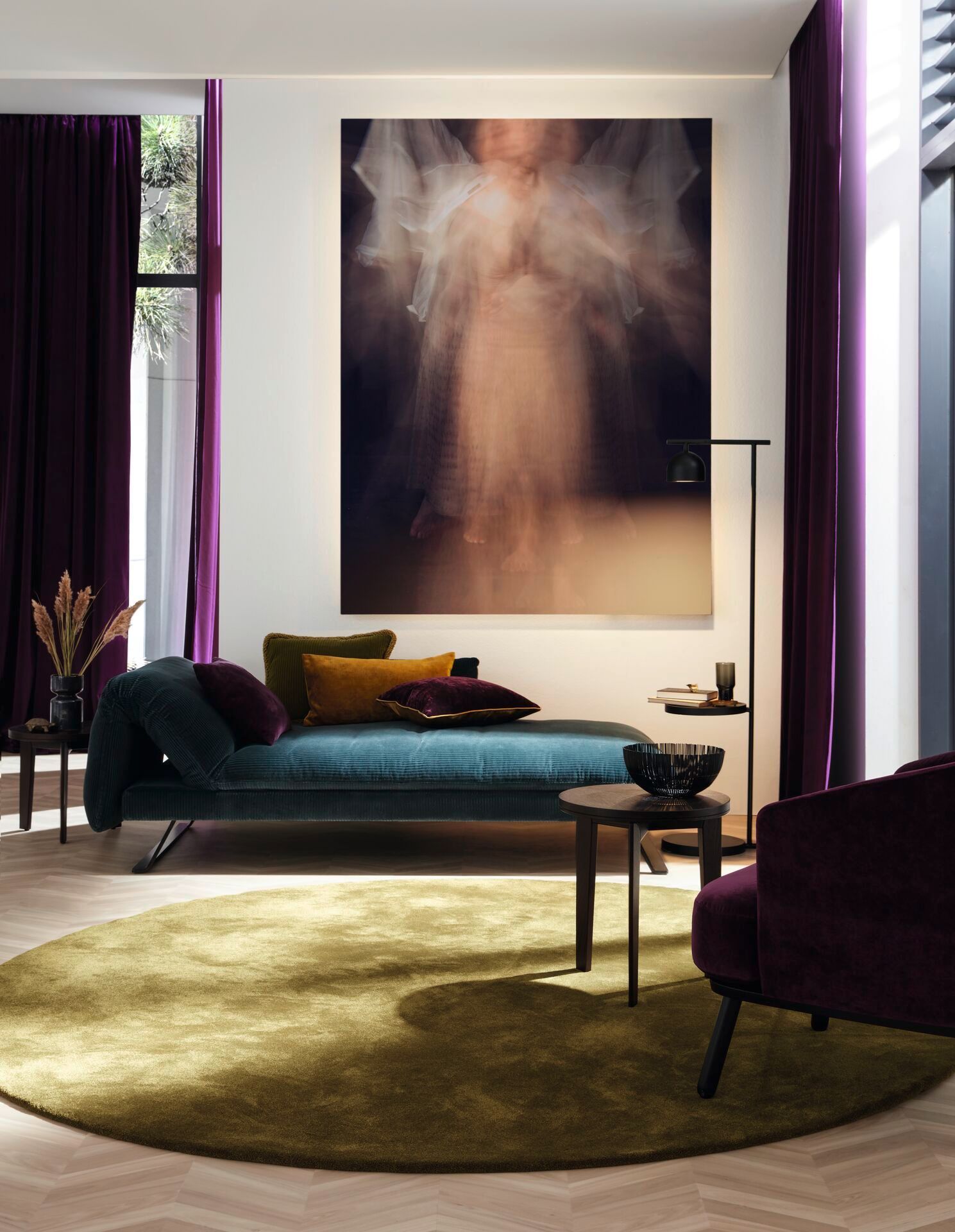 Elegantes Wohnzimmer mit petrolfarbenem Teppichboden und Samtliege, stimmige Deko in warmen Tönen.