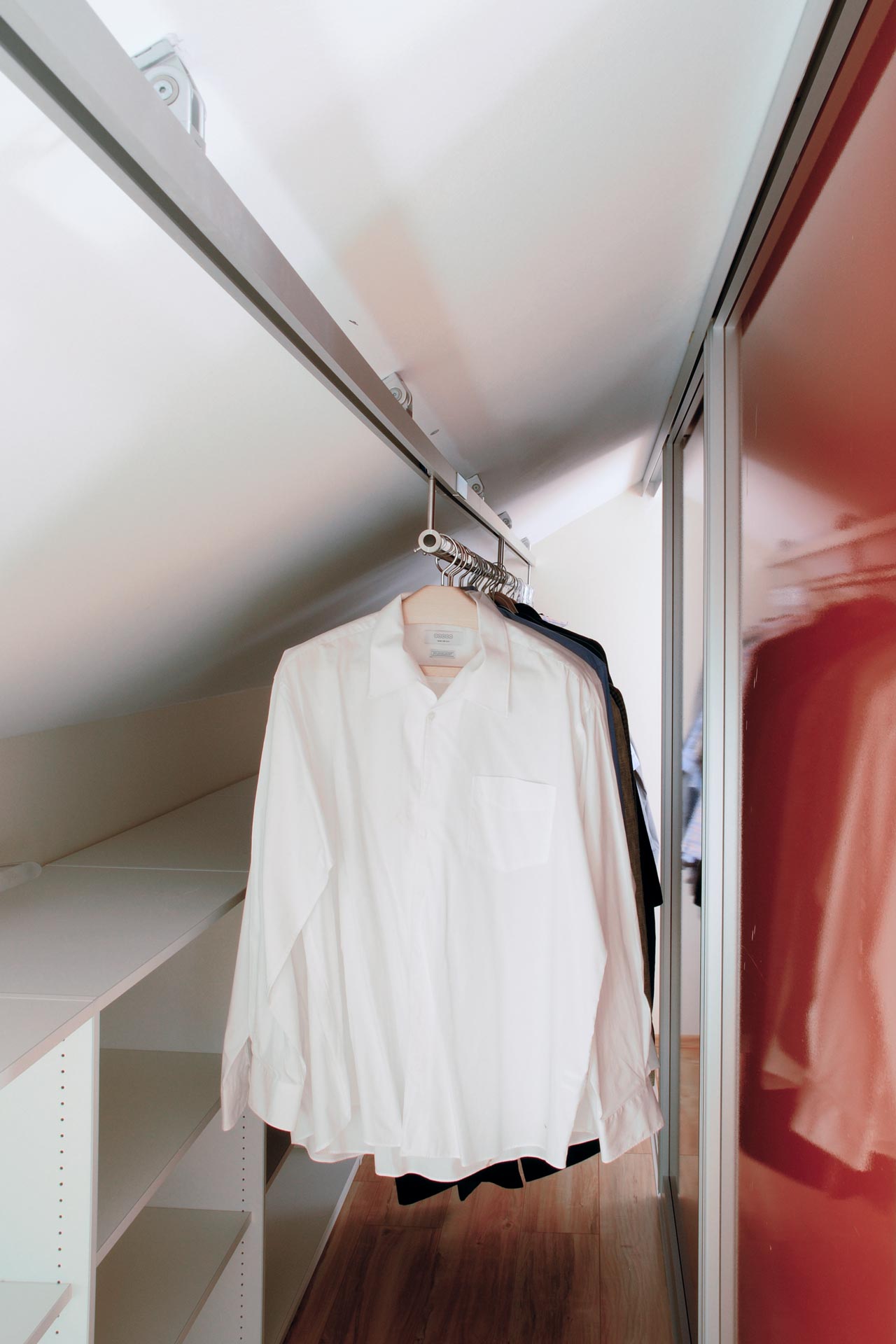 Der dressglider, die verschiebbare Kleiderstange, hinter einem Schrank unter einer Dachschräge Der dressglider, die verschiebbare Kleiderstange, hinter einem Schrank unter einer Dachschräge
