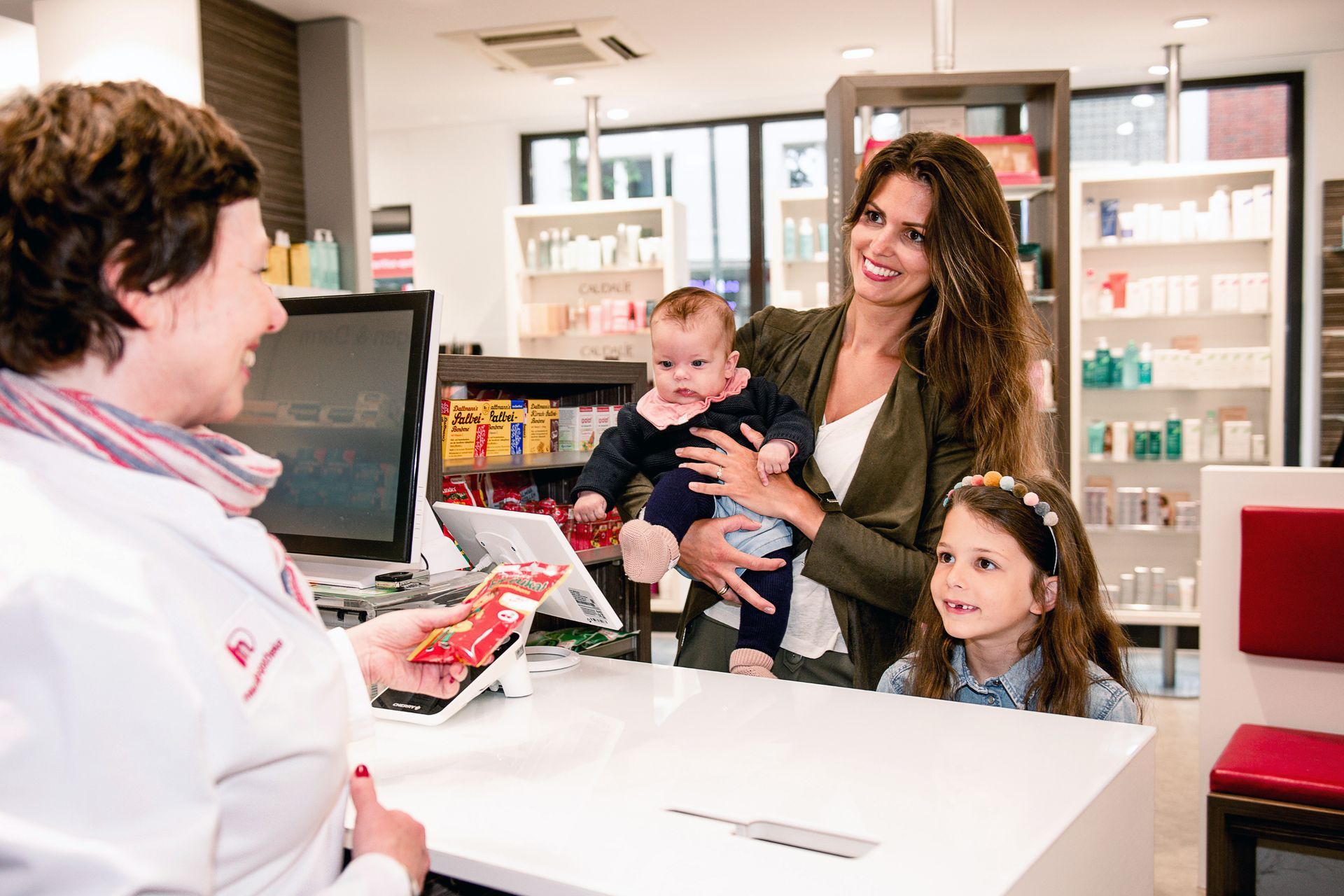 Apothekerin berät Mutter mit zwei Kindern an der Theke