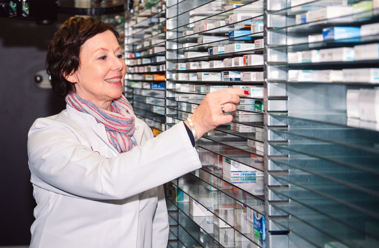Apothekerin entnimmt Medikamente aus Medikamentenregal