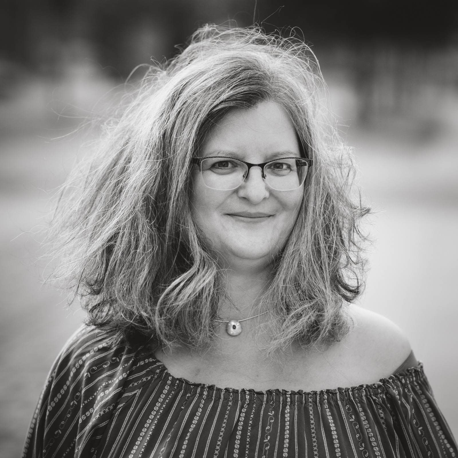 Foto by Maike Vará lächelden Frau mit Brille und langen, windzerzausten Haaren