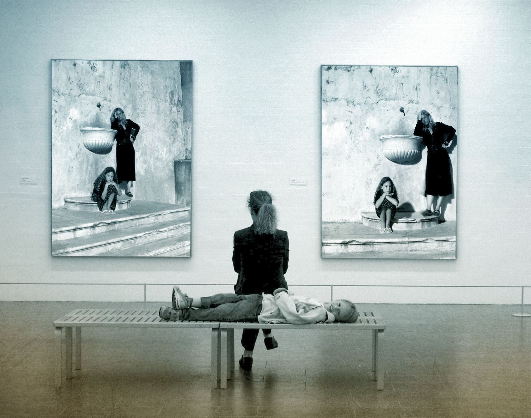 Sitzende Frau im Museum, wie sie zwei grosse Bilder vor ihr betrachtet