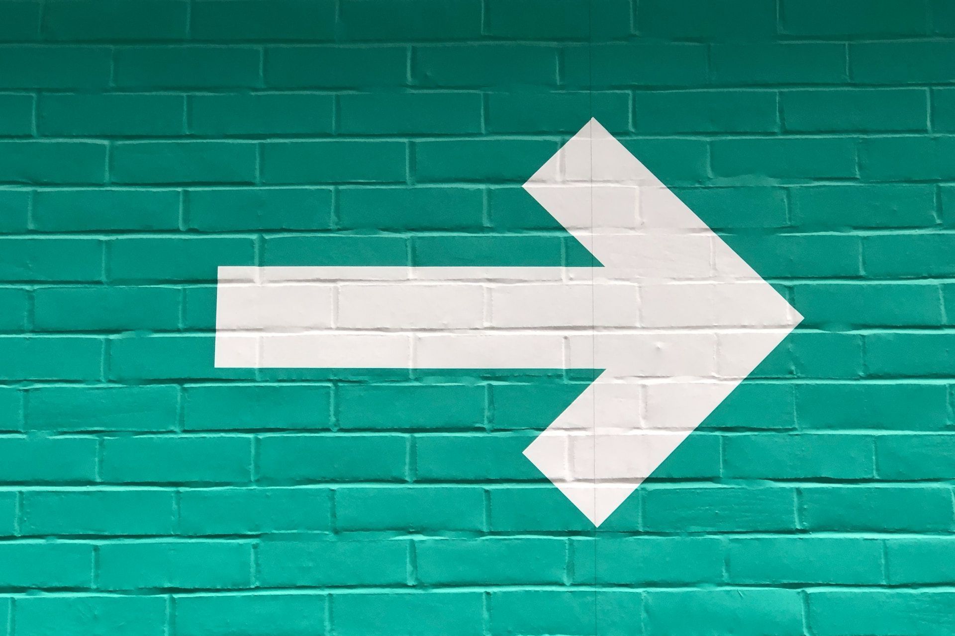 Weisser Pfeil auf eine grün gestrichene Backsteinwand