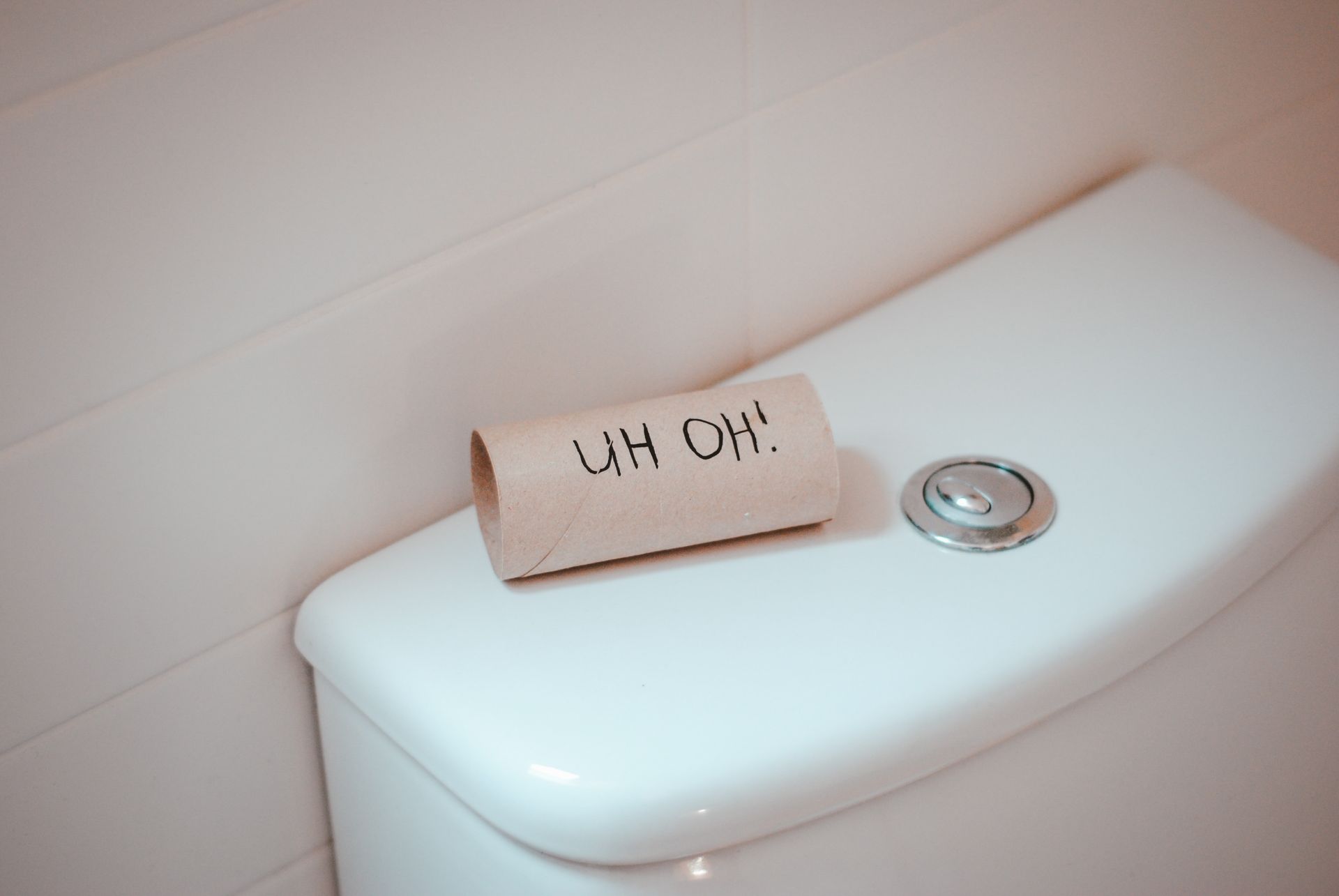 An empty toil roll sitting on top of the toilet cistern with the words Uh Oh! written on it.