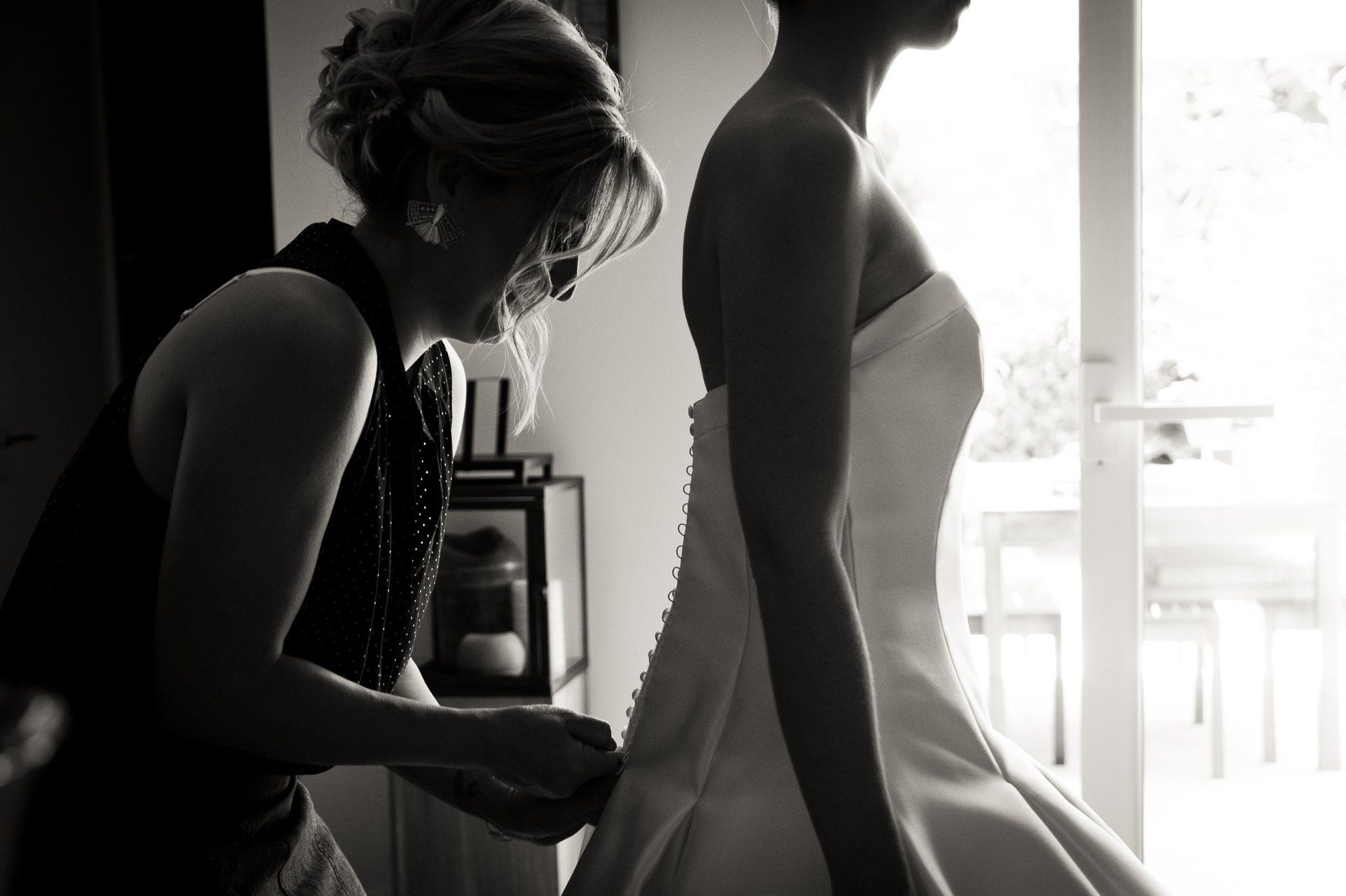 Photographie de mariage de Elizabeth Perrot Photo. Reportage pendant les préparatifs de la mariée. Habillage de la mariée. La témoin aide la mariée à enfiler sa robe de mariée. Mariage à St Cyr au Mont d'Or, Monts d'Or, environs de Lyon, Rhône, Rhône-Alpes, France.