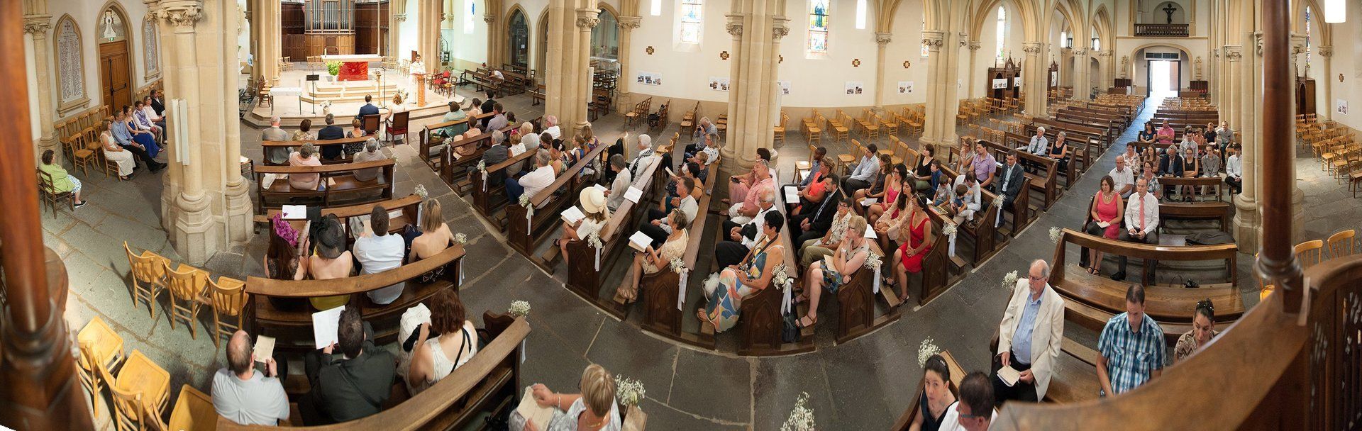 Photographie de mariage de Elizabeth Photo. Cérémonie religieuse, panoramique des mariés et de leurs invités dans l'église. Mariage à Roanne, Loire, Rhône Alpes, France.