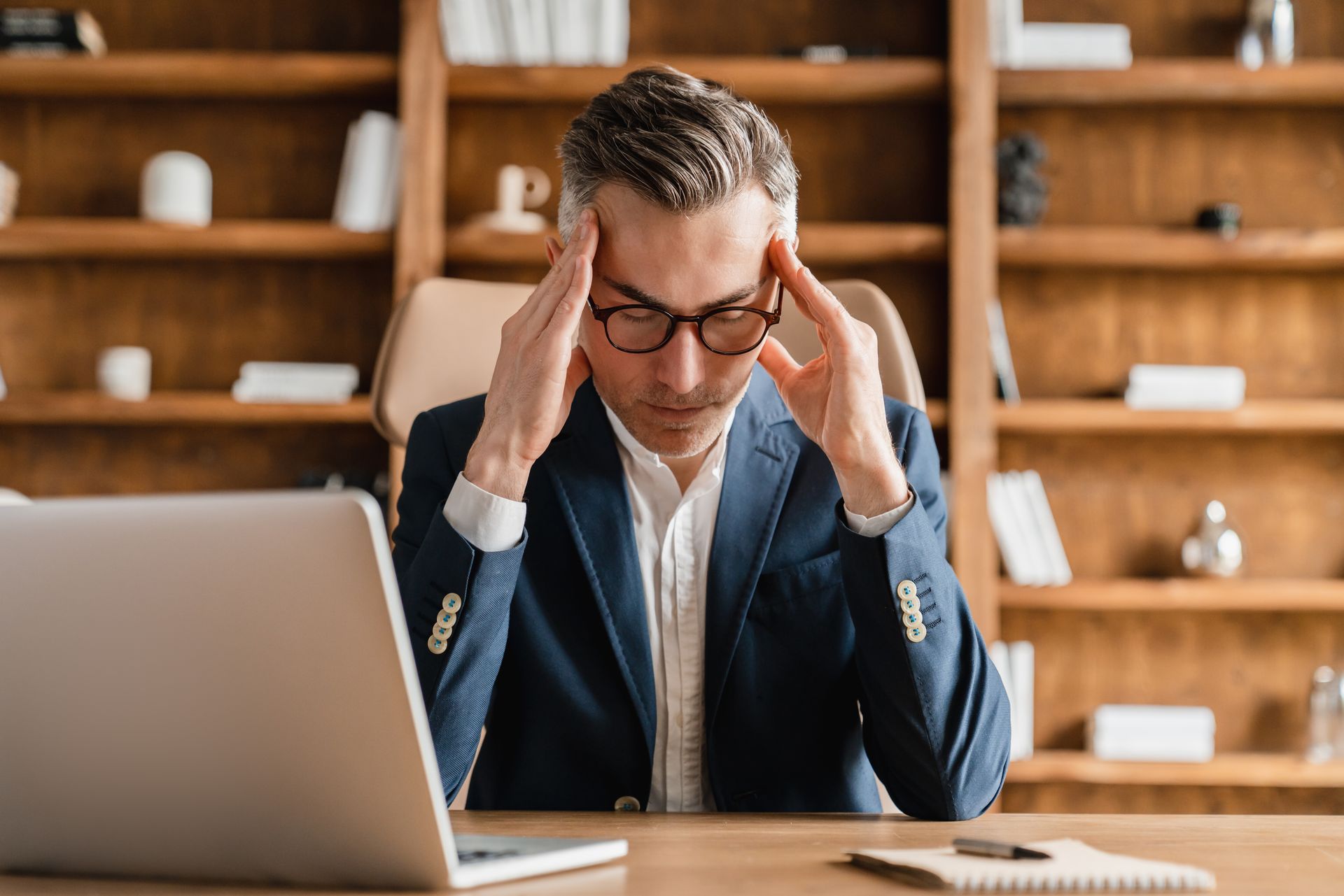 Man sitting at his desk looking frustrated and stressed while working on his laptop.
