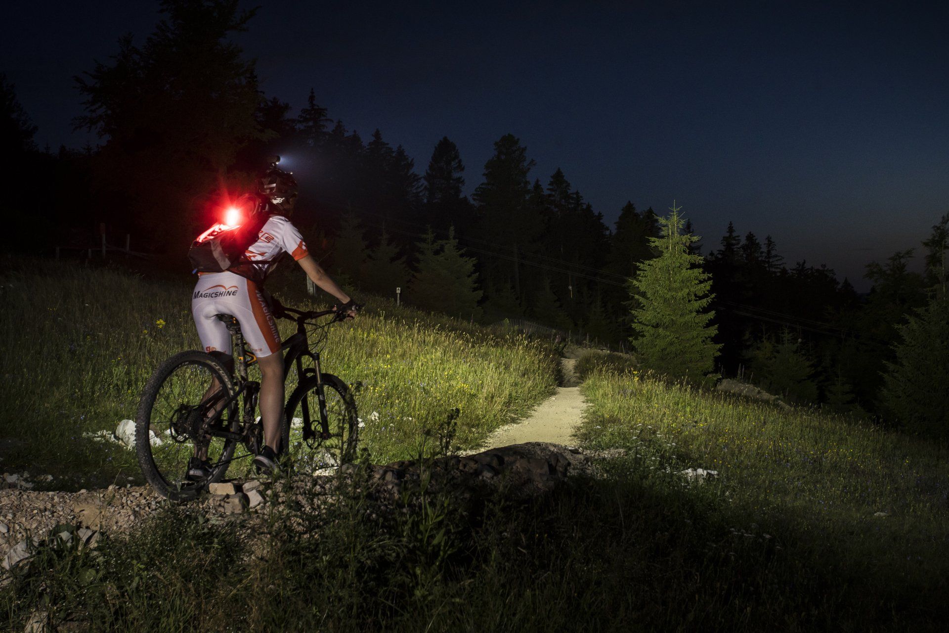 Magicshine Helmlampe Monteer 6500 mit 6 Leuchten bei Sonnenuntergang im Wald und auf der Wiese mit dem Fahrrad oder Mountainbike, offroad inklusive Rücklicht des Fahrradfahrers SeeMee 180 im Trailpark