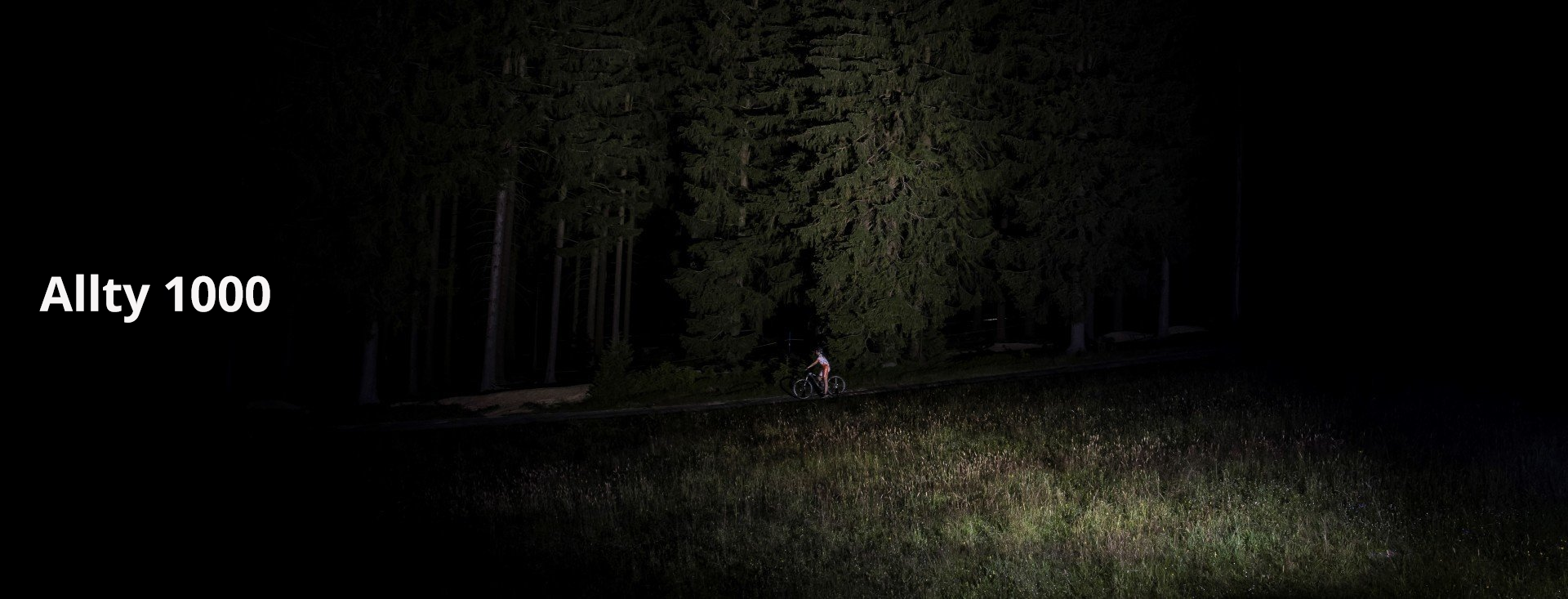 Magicshine LED Stirnlampe Allty 1000 mit Fahrradfahrer auf Wiese vor Wald und starkem LED Lichtkegel