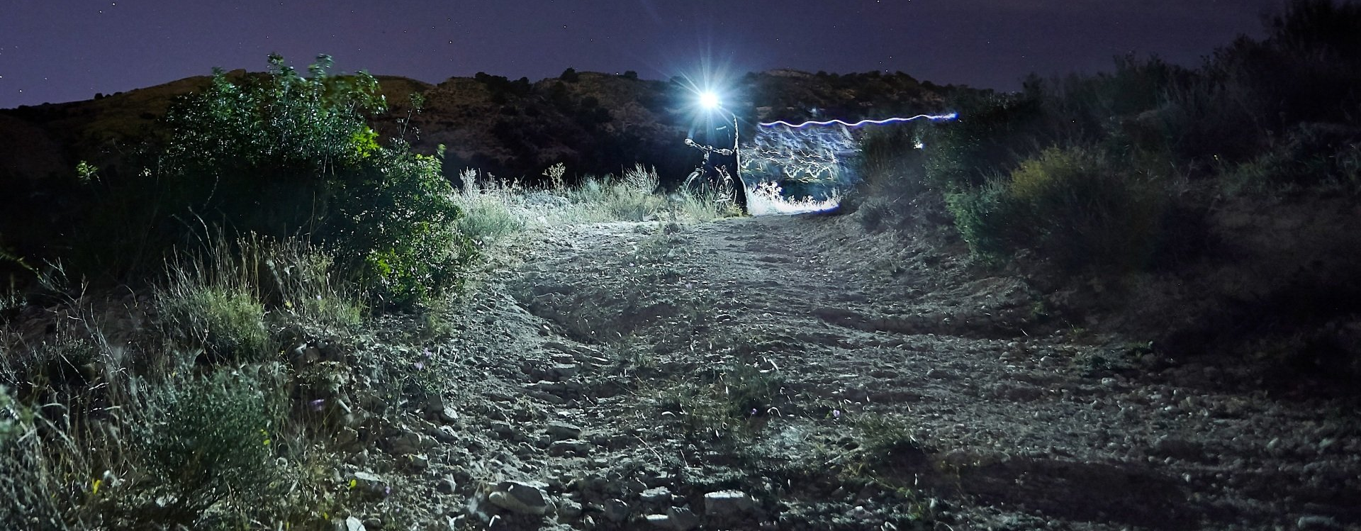 Magicshine LED Stirnlampe Allty 600 mit Fahrradfahrer auf Wiese vor Wald und starkem LED Lichtkegel