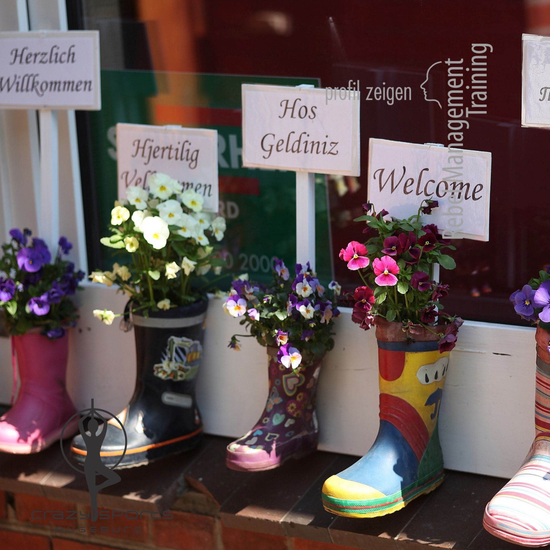 Gummistiefel mit Blumen und Willkommensschildern in verschiedenen Sprachen
