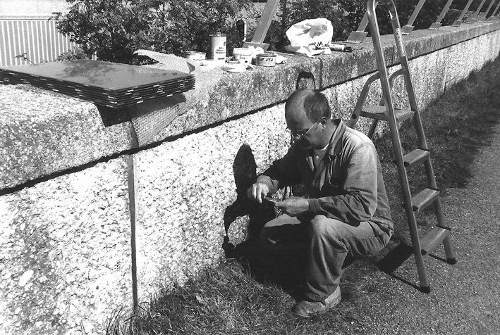 Mann in Arbeitskleidung und in Hocke vor Mauer, verschiedenes Arbeitsgerät