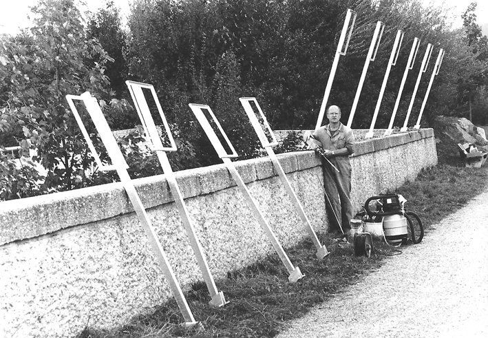 Mann in Arbeitskleidung vor Mauer, Metallteile und Arbeitsgerät