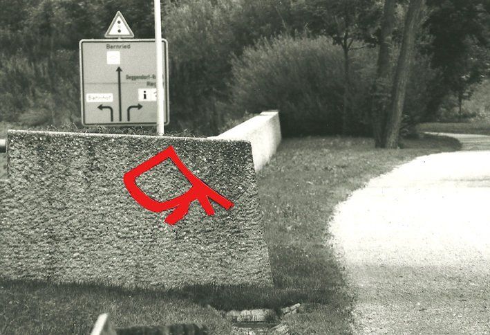 Rotes Zeichen an Mauer, im Hintergrund Verkehrszeichen