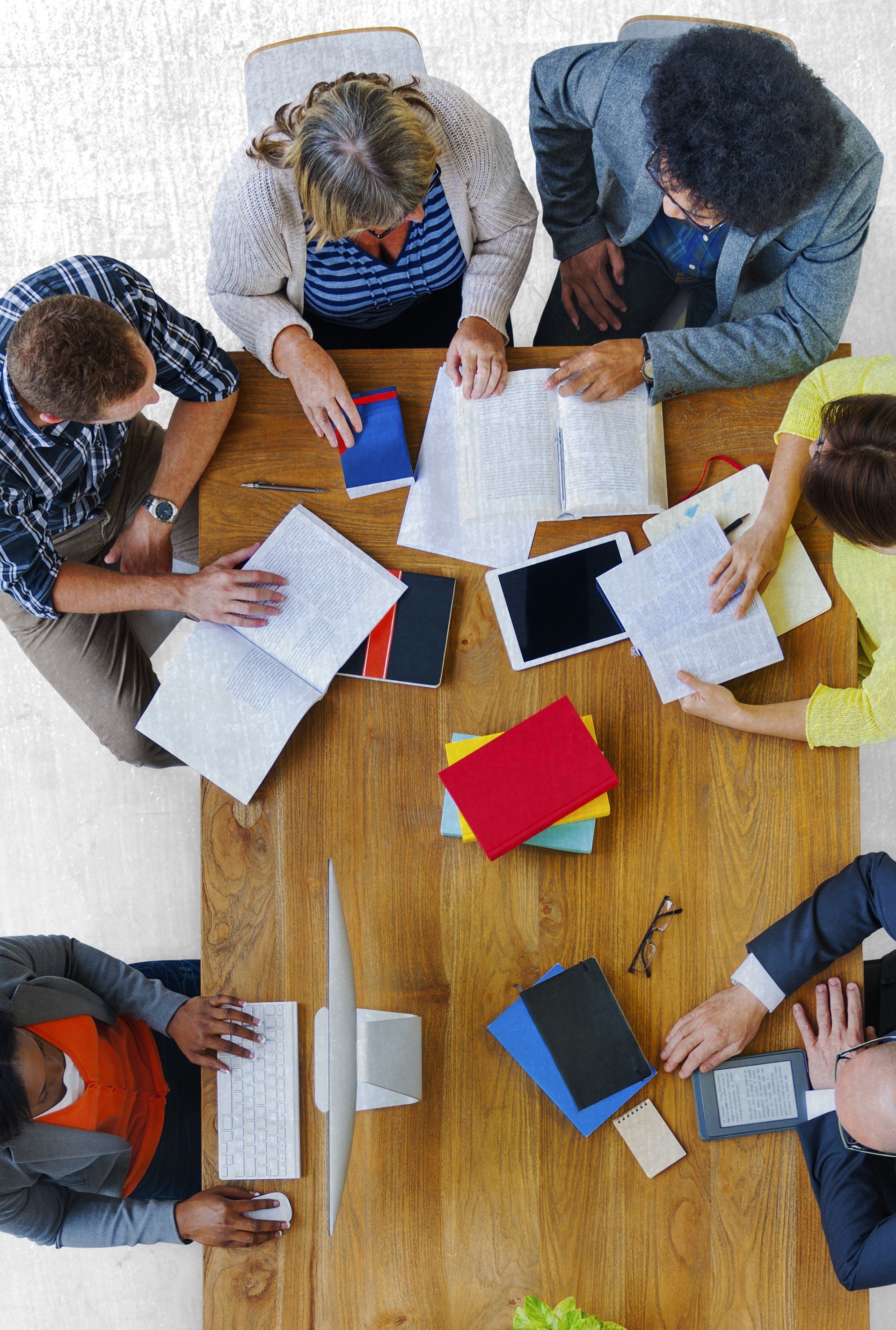 aerial view of people seated around a table with books and tablets out working.
