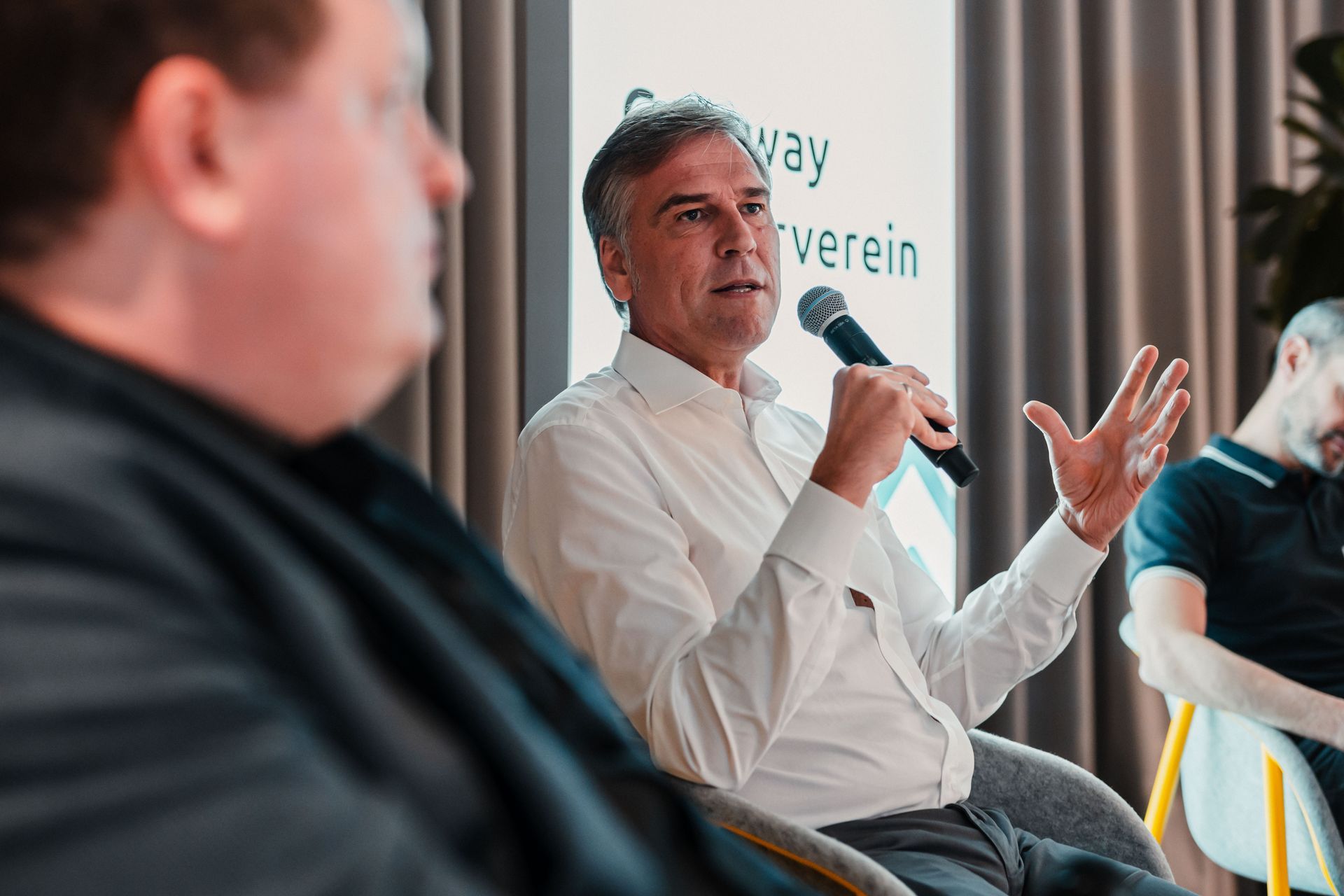 Ein Mann spricht mit einem Mikrofon während einer Podiumsdiskussion. Im Vordergrund sitzen weitere Teilnehmende, ein Banner mit der Aufschrift „Gateway Förderverein“ ist sichtbar.