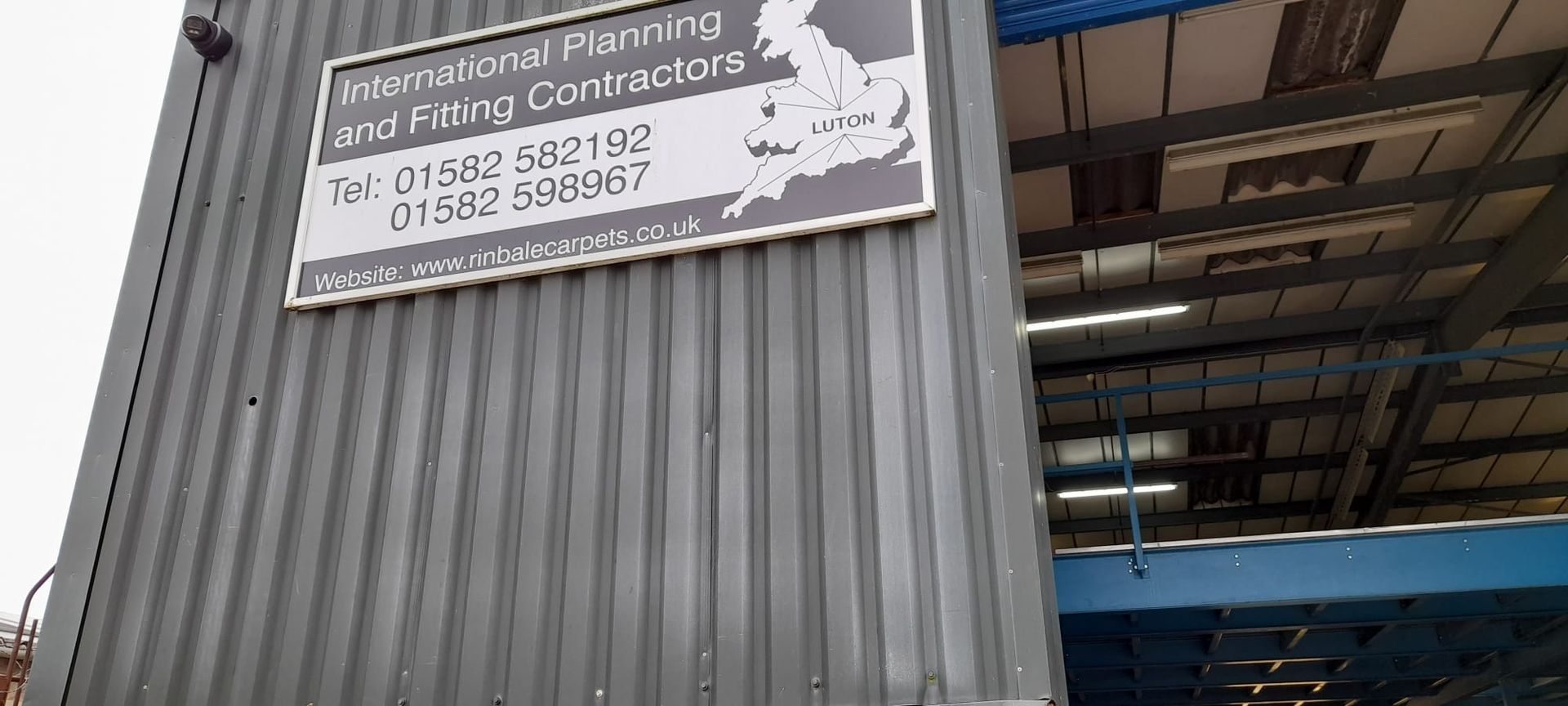 A Hikvision 8mp ip camera on warehouse with a large sign reading 'International Planning and Fitting Contractors