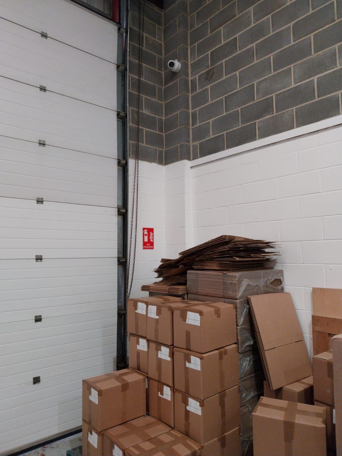 Hikvision dome camera installed inside a warehouse above stacked cardboard boxes near a fire exit.