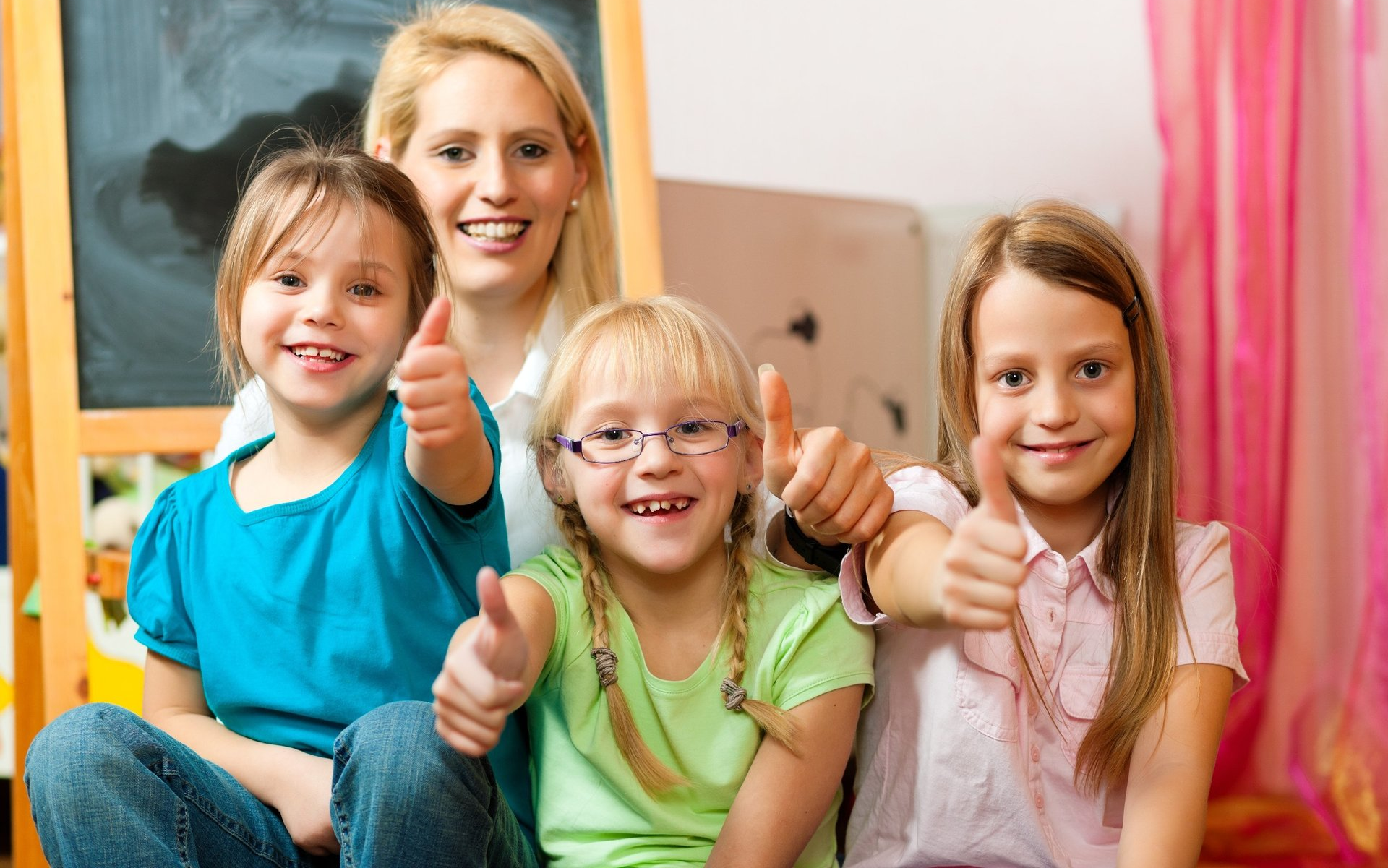 Tre bambine e una maestra in primo piano e una lavagna sullo sfondo