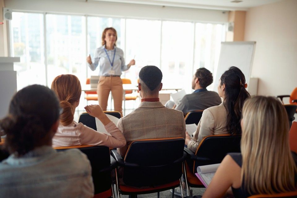 Un'insegnate che fa lezione in un'azienda, davanti a un gruppo di persone che sono sedute ad ascoltare