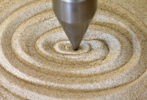 Hypnose als Therapieinstrument. Ein metallenes Pendel malt Kreise in Sand.