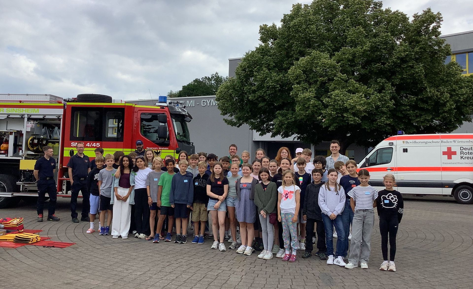 Schülerinnen und Schüler sowie Mitarbeiter von Feuerwehr und Rotem Kreuz samt Einsatzfahrzeugen