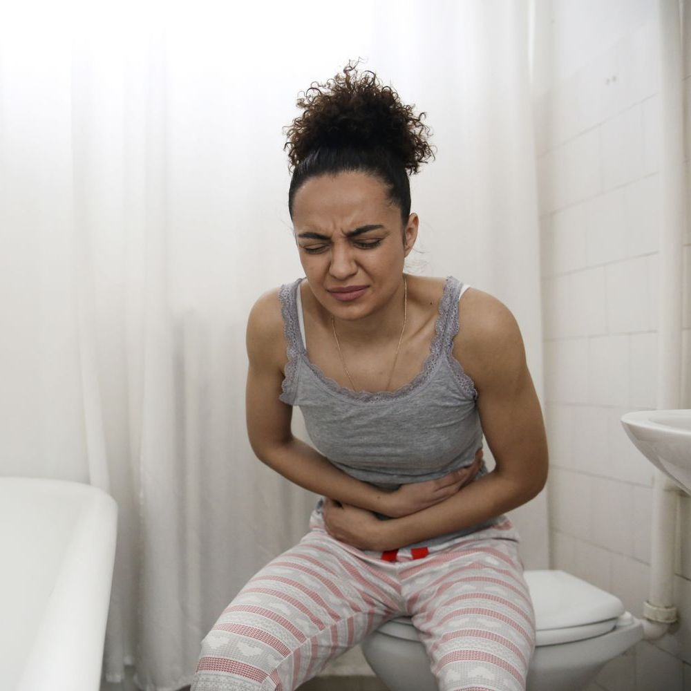 woman on toilet holding belly in pain