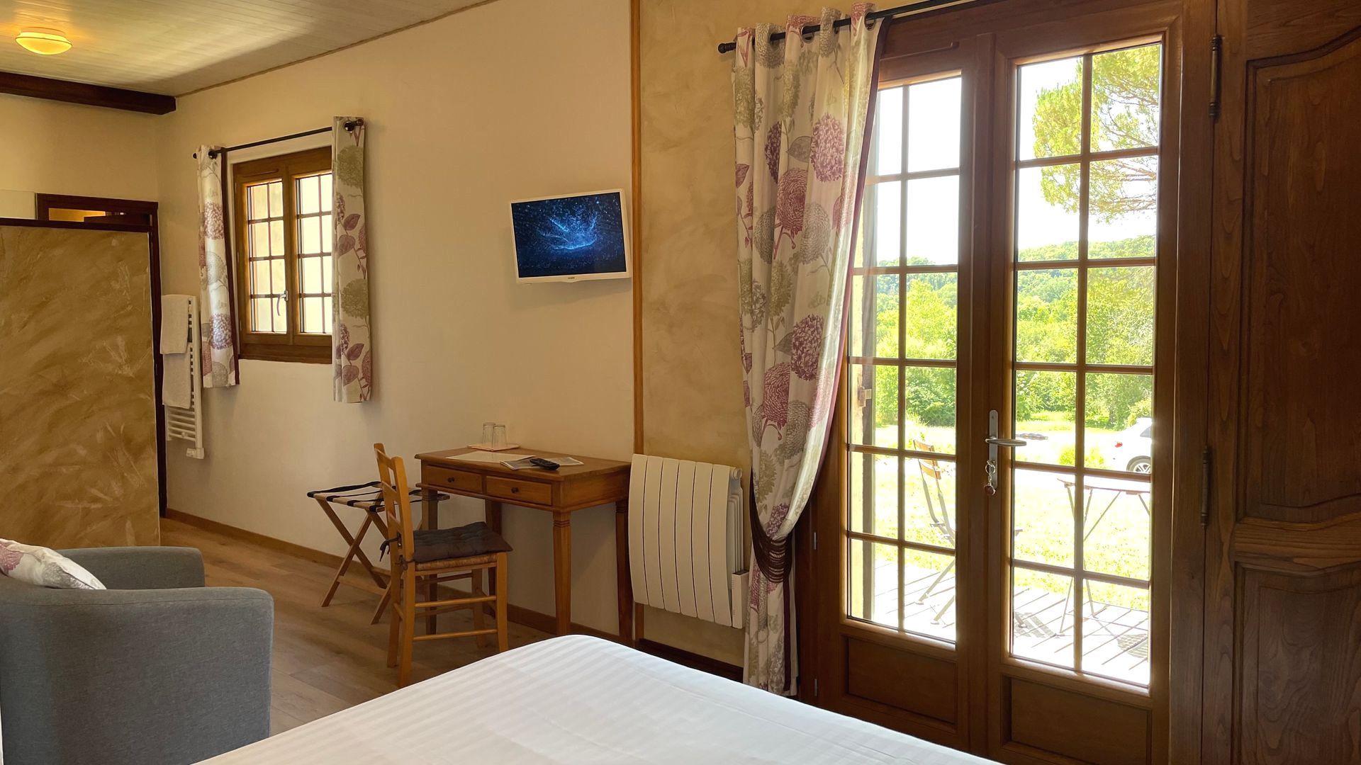 Chambre Sérénité, lit, table, chaise, télévision murale, porte fenêtre donnant sur le parc.