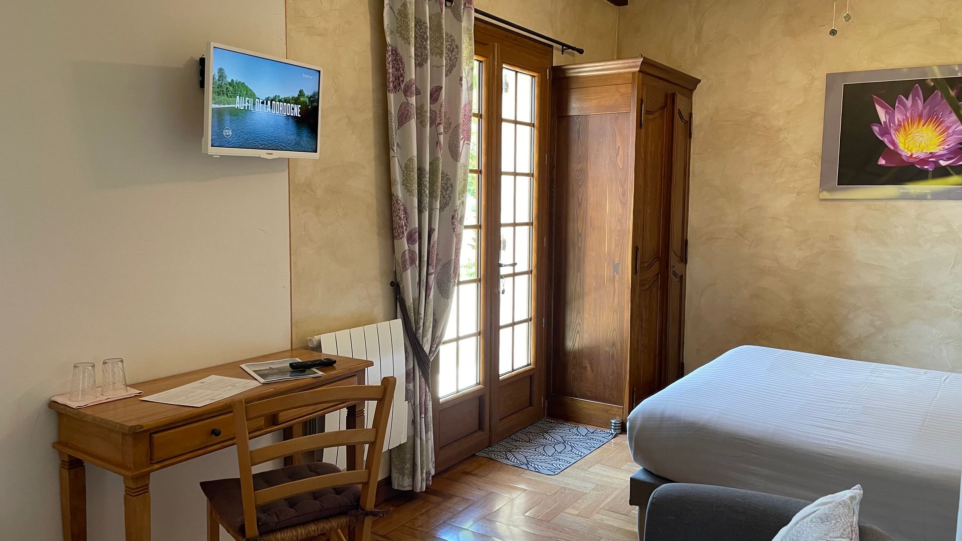 Chambre Sérénité, lit, table et chaise, télévision murale, porte fenêtre avec vue donnant sur le parc.