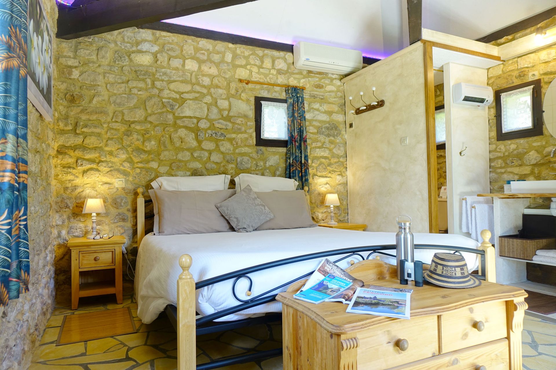 Inside view bedroom La Borie, bed with white linen, small table and wall stone