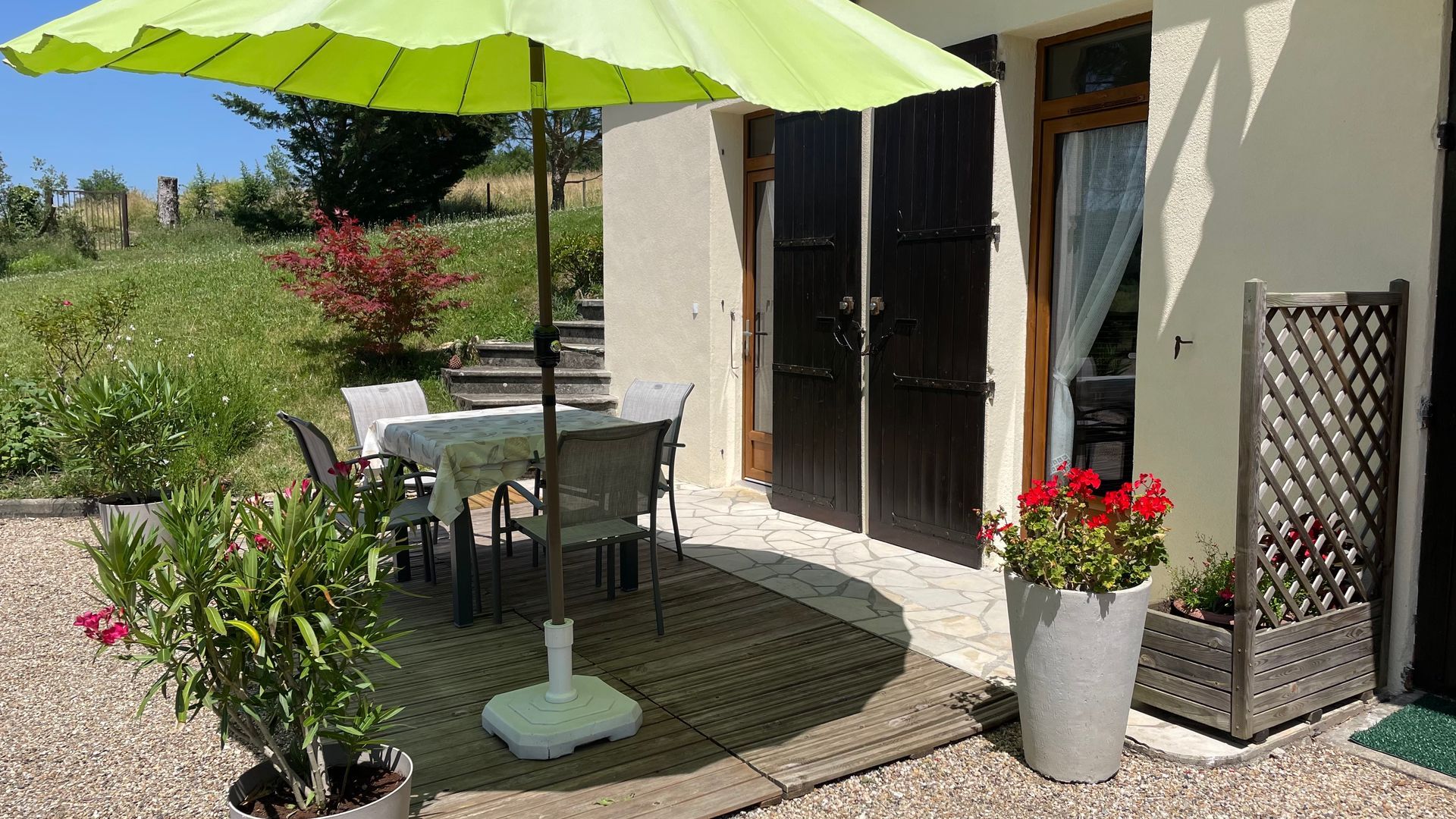 Terrasse et entrée du gîte avec table carrée, chaises et parasol