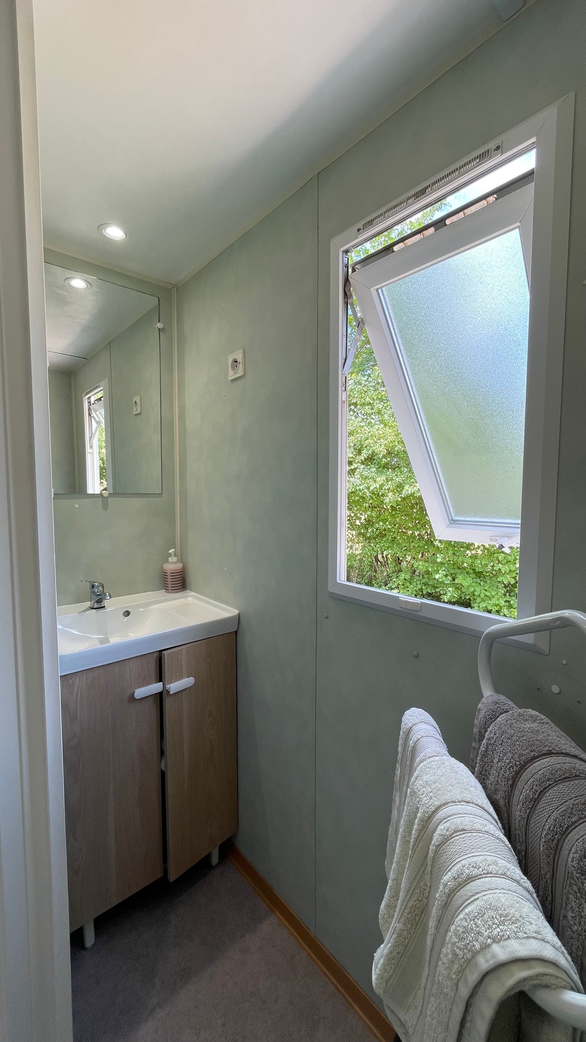 Salle de bain avec serviettes, lavabo et fenêtre donnant sur le jardin