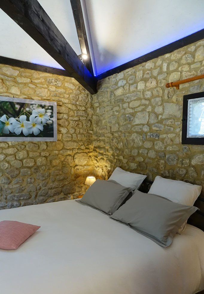 Vue intérieure de la chambre La Borie avec lit en 160x200cm, photograhie murale avec fleurs blanches (frangipanier) lumières colorées bleu au plafond et dorée sur la table de chevet.